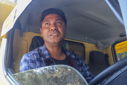 A man with a friendly expression sits in the driver's seat of a vehicle.