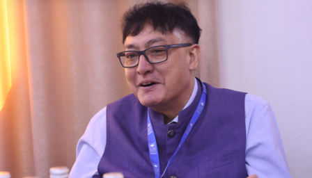 Smiling man in glasses wearing a purple vest, sitting at a table with soft lighting.