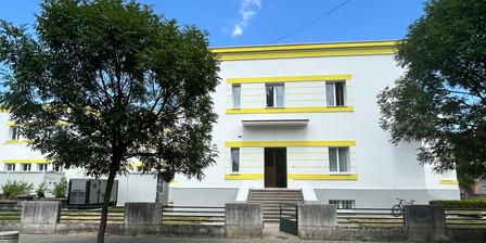 Modern white building with yellow accents, surrounded by trees and clear blue sky.