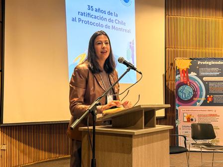 Woman speaking at a podium during an event, with a presentation screen behind her.