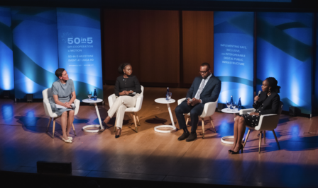 Panel discussion on a stage with five people seated in chairs, blue backdrop.