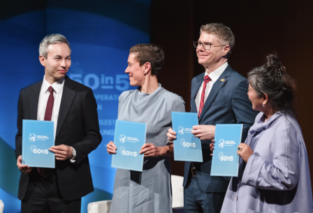Four professionals on stage at a conference, each holding a blue booklet.