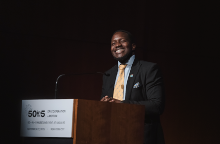 Photograph of a man in a suit giving a talk at a microphone podium, lectern placard visible.