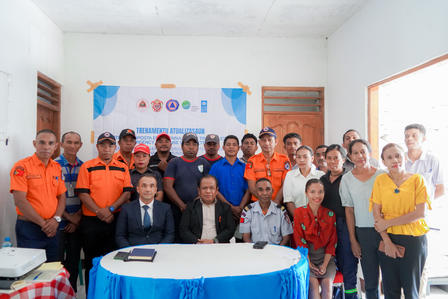 Photograph of a group posing in a meeting room; several in orange uniforms, banner on wall.