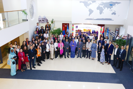 Group photo of diverse people in a bright atrium with a world map mural.