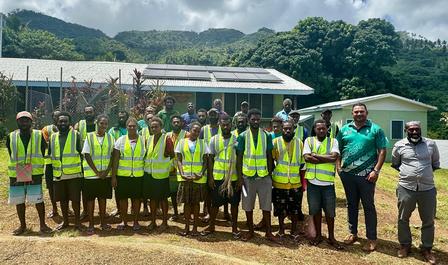 Group of people in high-visibility vests posing outdoors with mountains in the background.