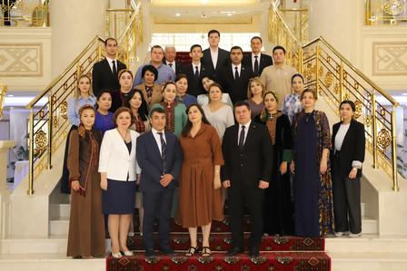 Group photo of men and women in formal attire on a staircase with gold railings and red carpet.