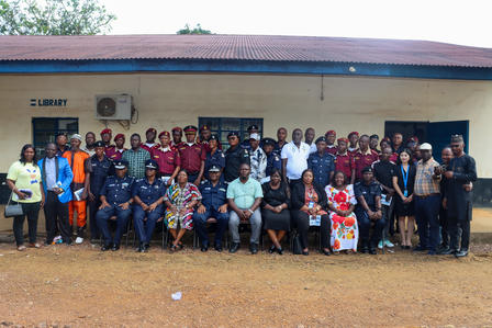 Large group of people posing in front of a small library building in a dusty yard.