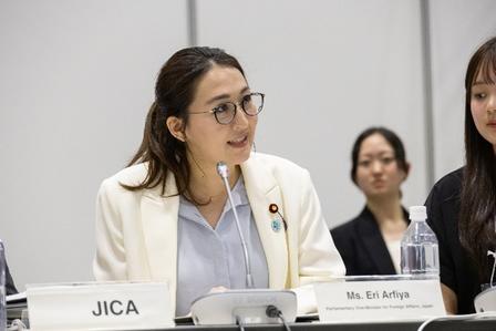 Panel discussion; woman in white blazer at center with microphone, JICA nameplate.