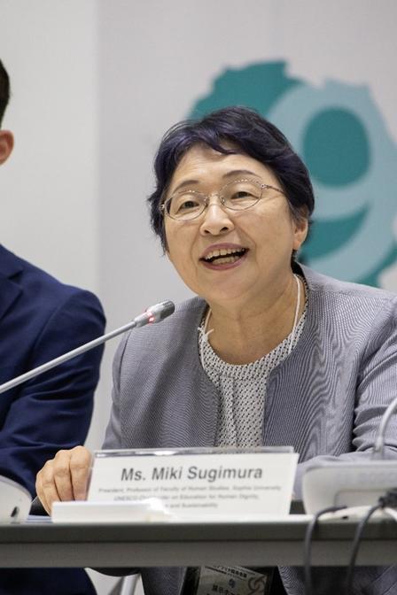 Panelist with short dark hair in gray blazer, seated at a table with microphone; name card reads Ms. Miki Sugimura.