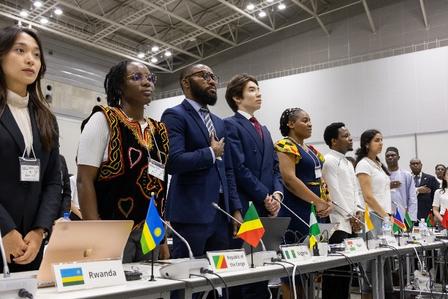 Diverse officials stand behind a long table with small country flags in a conference hall.