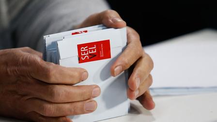 Photograph of hands holding a small gray box with a red label.
