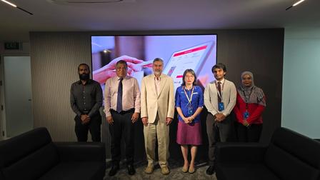 Seven people stand in a conference room in front of a large screen.