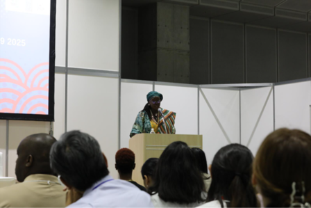 Photograph of a speaker at a podium addressing an audience in a conference hall.