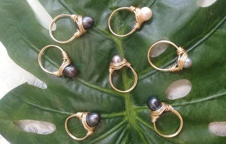 Gold rings with pink, black, and pearl beads arranged on a green leaf.