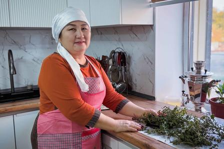 Person wearing orange sweater and pink apron stands at kitchen counter with fresh herbs.