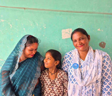 Three people in a green-walled room; left in blue veil, middle child, right in a patterned robe.