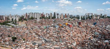 Dense cityscape with red-tiled rooftops in foreground and modern high-rises against a blue sky.