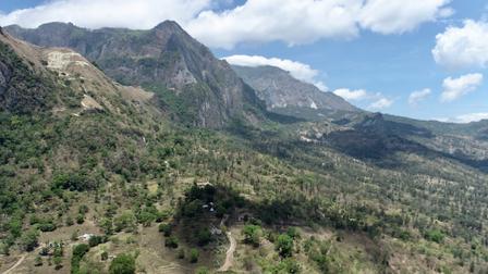 Mountain valley with green hills and rugged slopes under a blue, cloud-filled sky.