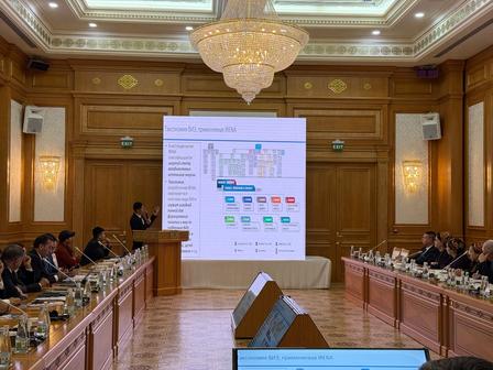 Formal conference room with wood paneling and a chandelier, attendees, and a projector slide.
