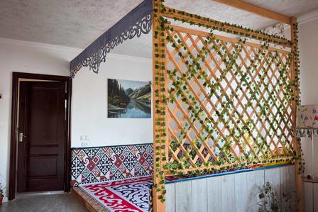 Photo of a room with a wooden door, lattice divider, red patterned rug, and wall painting.