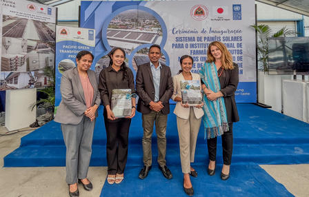 Five people stand on a blue carpet at a trade show, holding certificates with banners behind.