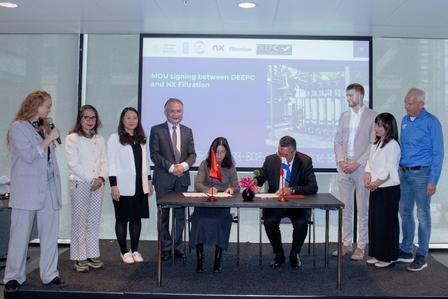 Group of professionals at a signing ceremony; two men seated signing documents.
