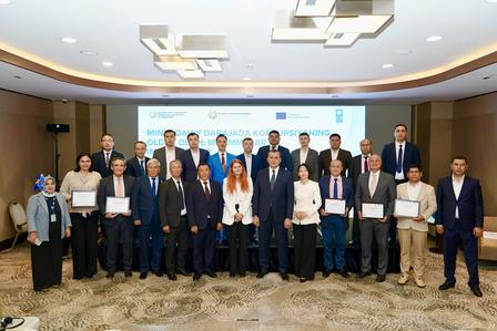 Group photo of professionals holding certificates at a conference in a meeting hall.