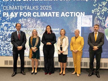 Six people in formal attire on a stage before a blue banner reading Play for Climate Action.