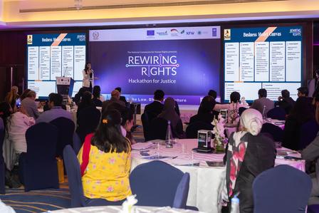 Audience at round tables watching a stage with a large Rewriting Rights banner.