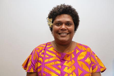 Photograph of a person in a pink and yellow geometric shirt, standing against a white background.