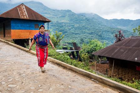Person in colorful clothes walks along a cobblestone path beside wooden mountain village houses.