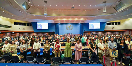 Group photo of attendees on stage in a conference hall with a blue backdrop.