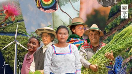 Group of people in hats pose at a colorful outdoor festival with banners and greenery.