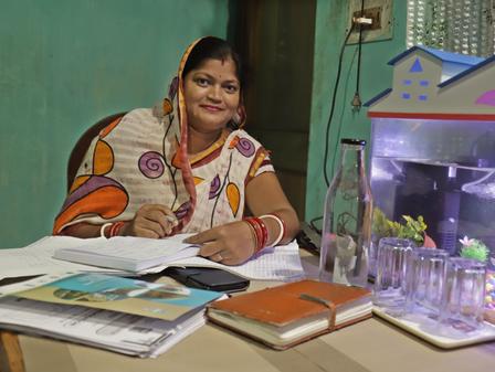 Person in a colorful patterned dress sits at a desk with papers; a small aquarium on the right.