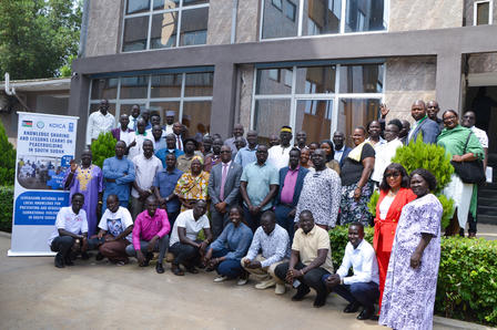 Photograph of a large diverse group posing outside a brick building with banners.