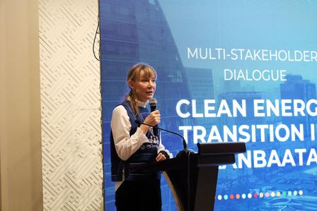 Female speaker at podium with a blue conference screen about clean energy transition.
