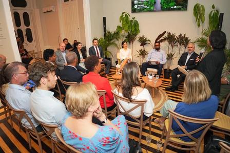 Photo: Group of people seated in a circle in a plant-filled room listening to a speaker.