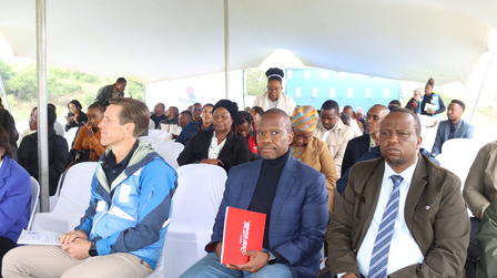 Audience under tent at an outdoor event; foreground man in suit with red folder.