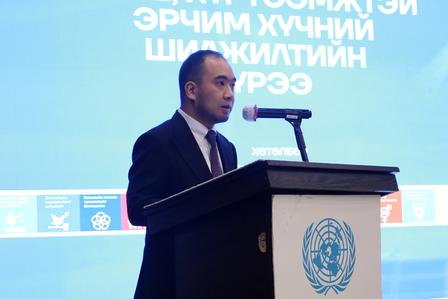 Man in suit giving a speech at a podium with UN emblem, blue backdrop.