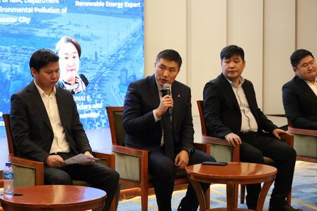 Panel of four men in suits on stage; center man speaks into microphone.