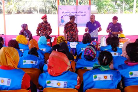 Outdoor training session under a canopy; presenters on stage and audience in blue vests.