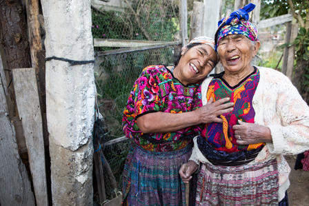 Two people in bright traditional clothing pose outdoors, smiling.