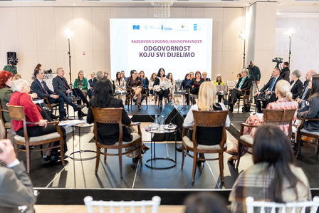 People seated in a circle in a bright conference room, presentation on a screen at the front.