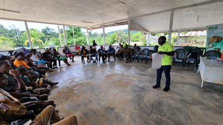 Presenter in neon vest leads training under a covered outdoor pavilion to a seated audience.