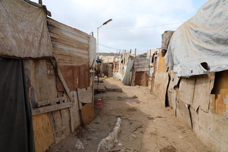 Dusty alley between tarp-covered shacks in a makeshift settlement.