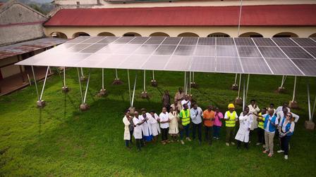 Group of people gathered on a grassy courtyard under a white arched canopy.