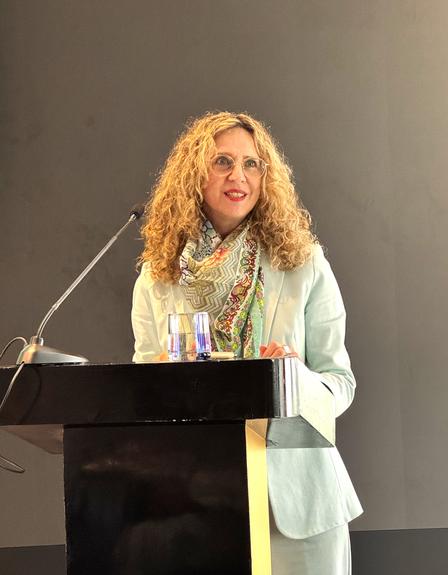 Speaker with curly hair in a light blazer at a podium on stage.