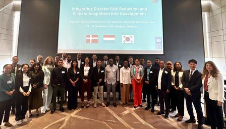 Group photo of diverse professionals posing on stage at a conference, blue slide in the background.