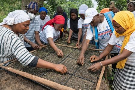 Group of people outdoors weaving a net on a wooden frame.